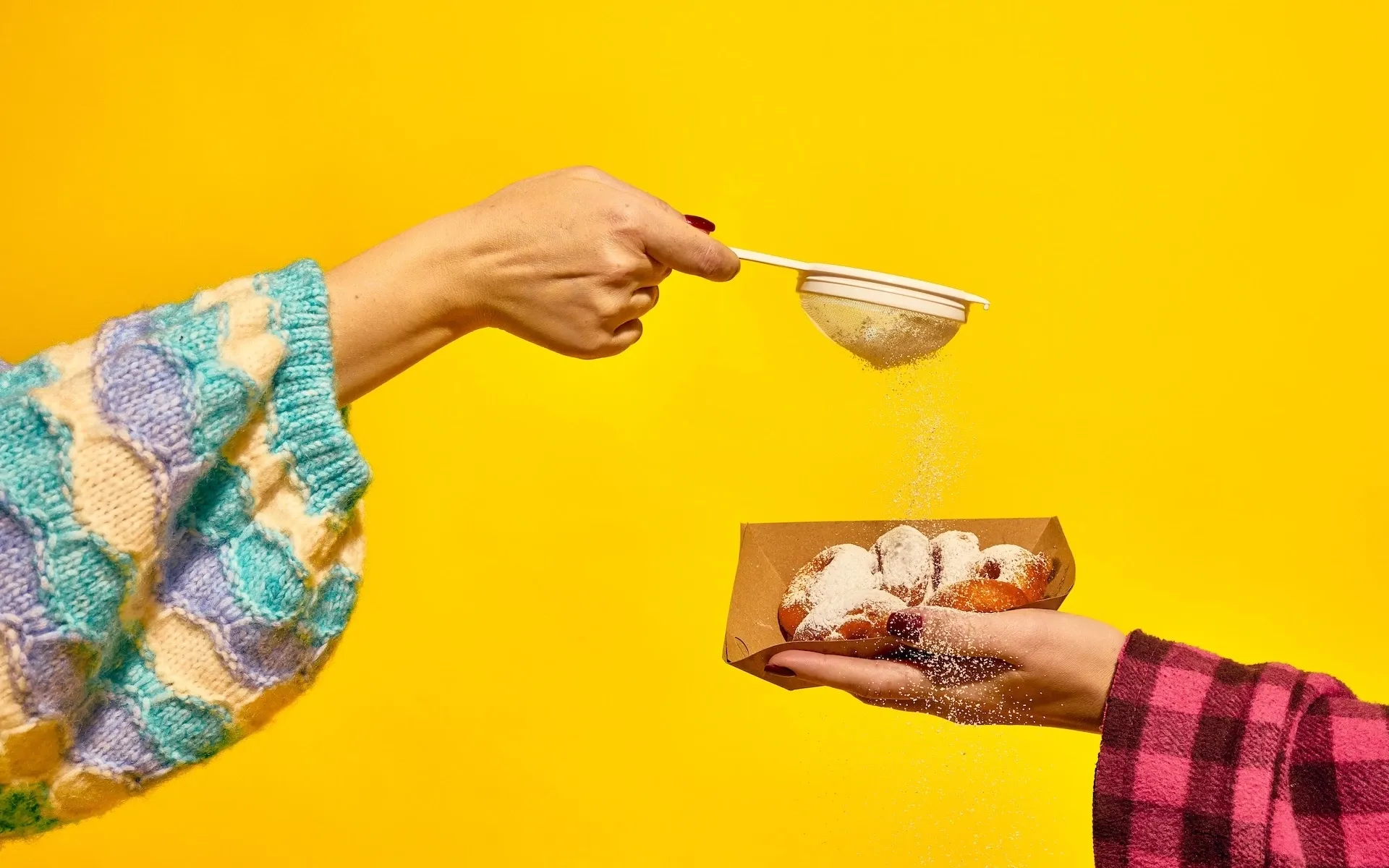 Two people dusting donuts with sugar